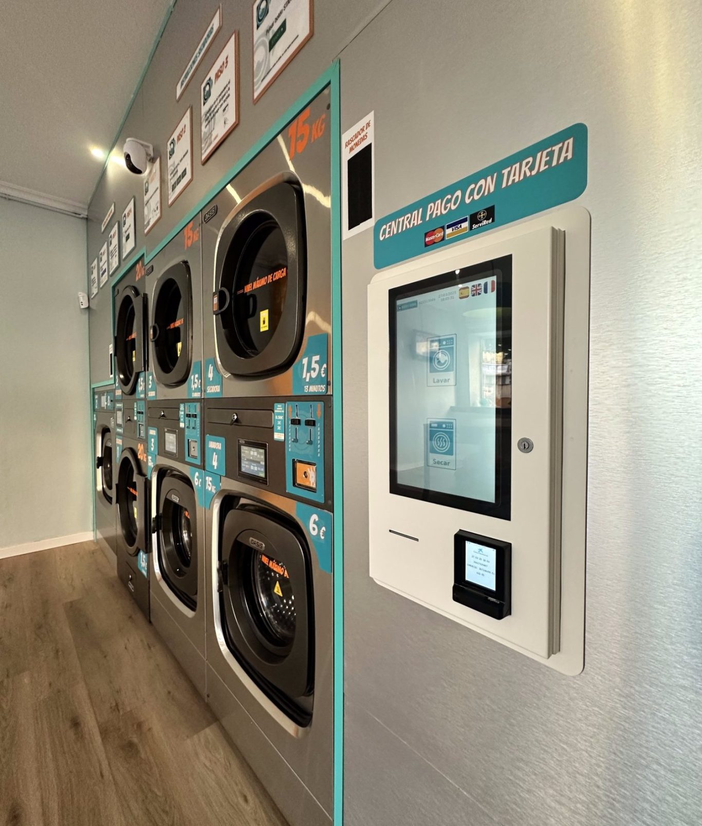 Pago con tarjeta Seco y Espuma Lavandería de autoservicio con máquinas de lavadoras y secadoras y un panel digital de pago con tarjeta.